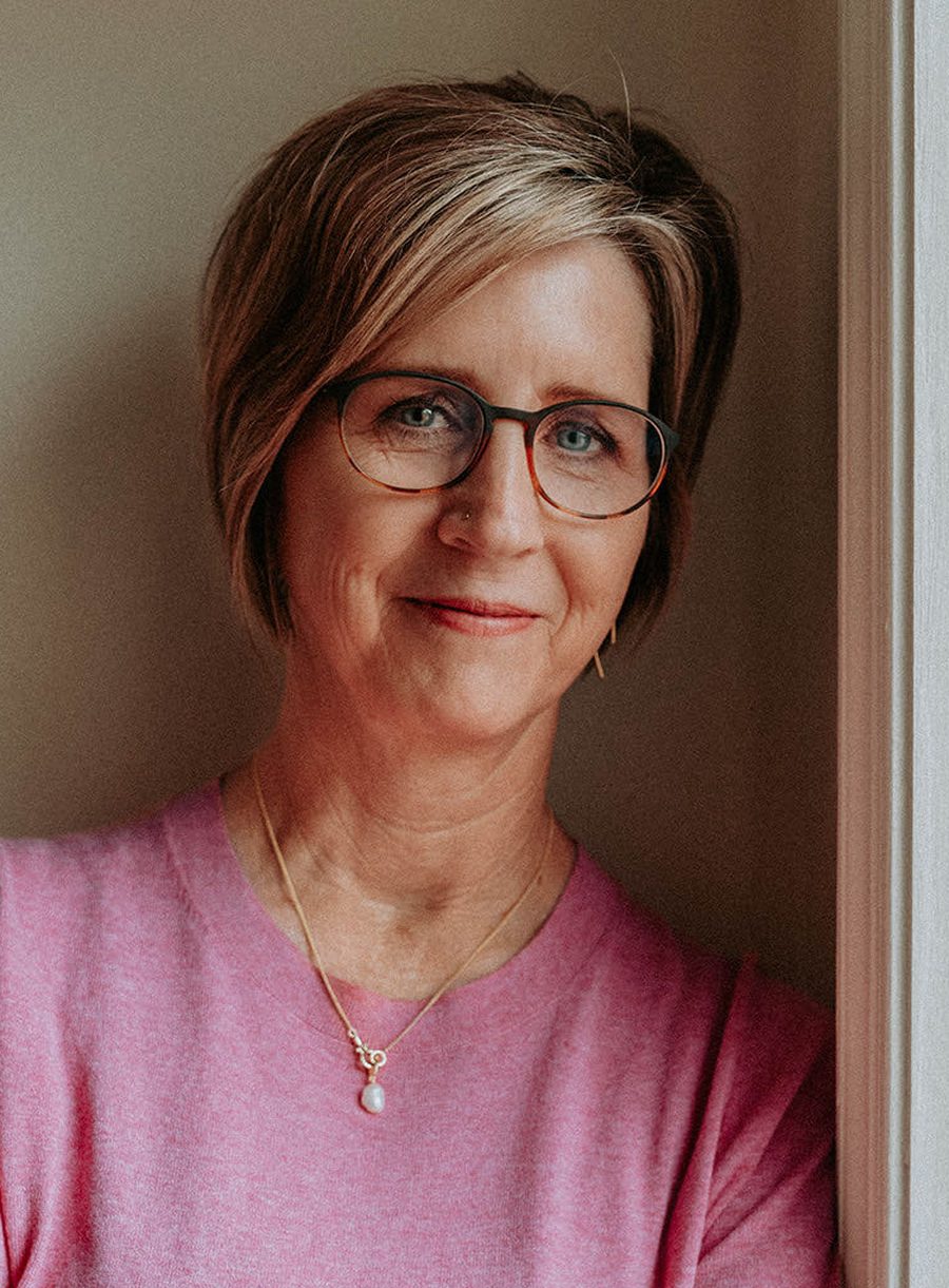 Kelly Wood, LCSW, smiling, wearing glasses and a pink sweater, leaning in a doorway.