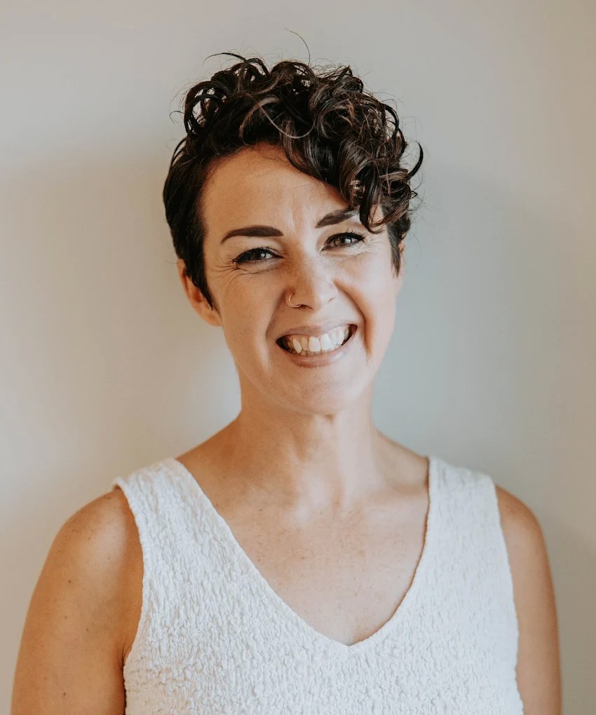 Joy Wawrzyniak, LCSW, laughing, in a white top against a soft grey-green wall.