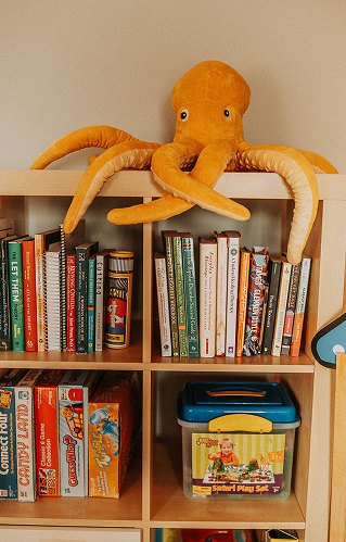 A shelf of board games and books in the play room, with a large orange stuffed octopus on top.