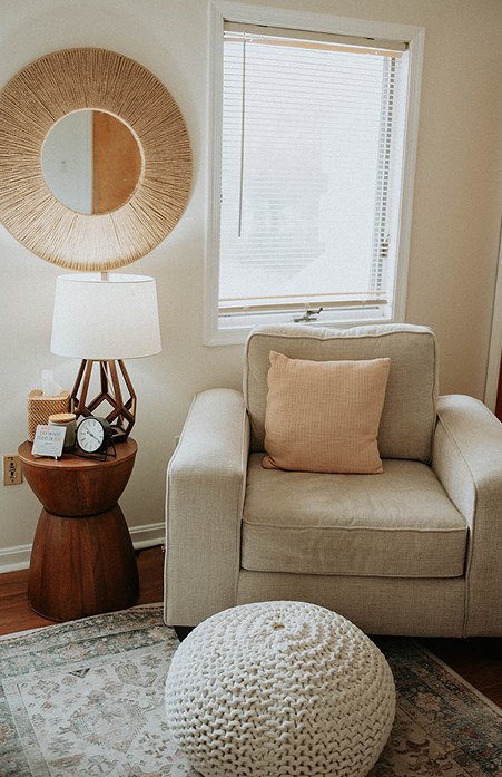 A Willow Tree therapy room with a soft armchair, a knitted floor pouf, a lamp and a sunlit window.
