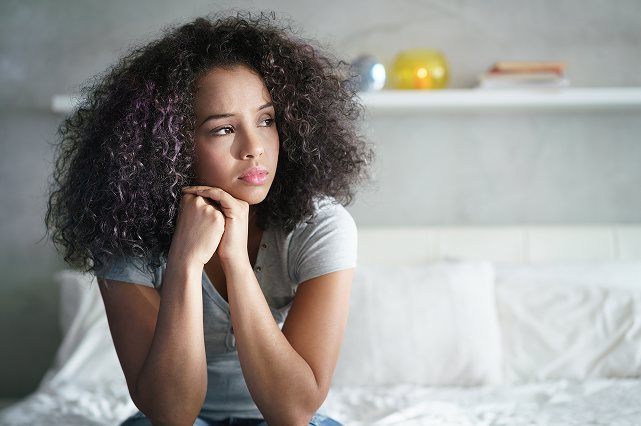 A teenage girl sitting on her bed, chin resting on her hands.