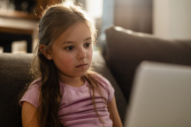 Pensive little girl using laptop while relaxing at home